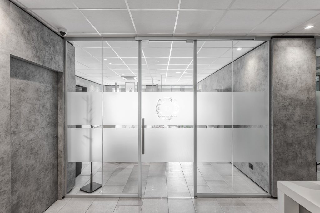 Vista Frontale degli Uffici Direzionali. In foto la parete realizzata con il sistema di pareti in cristallo Maisistem Glass. Le porte scorrevoli in vetro sono dotate di pellicole opache con il logo dell'azienda 