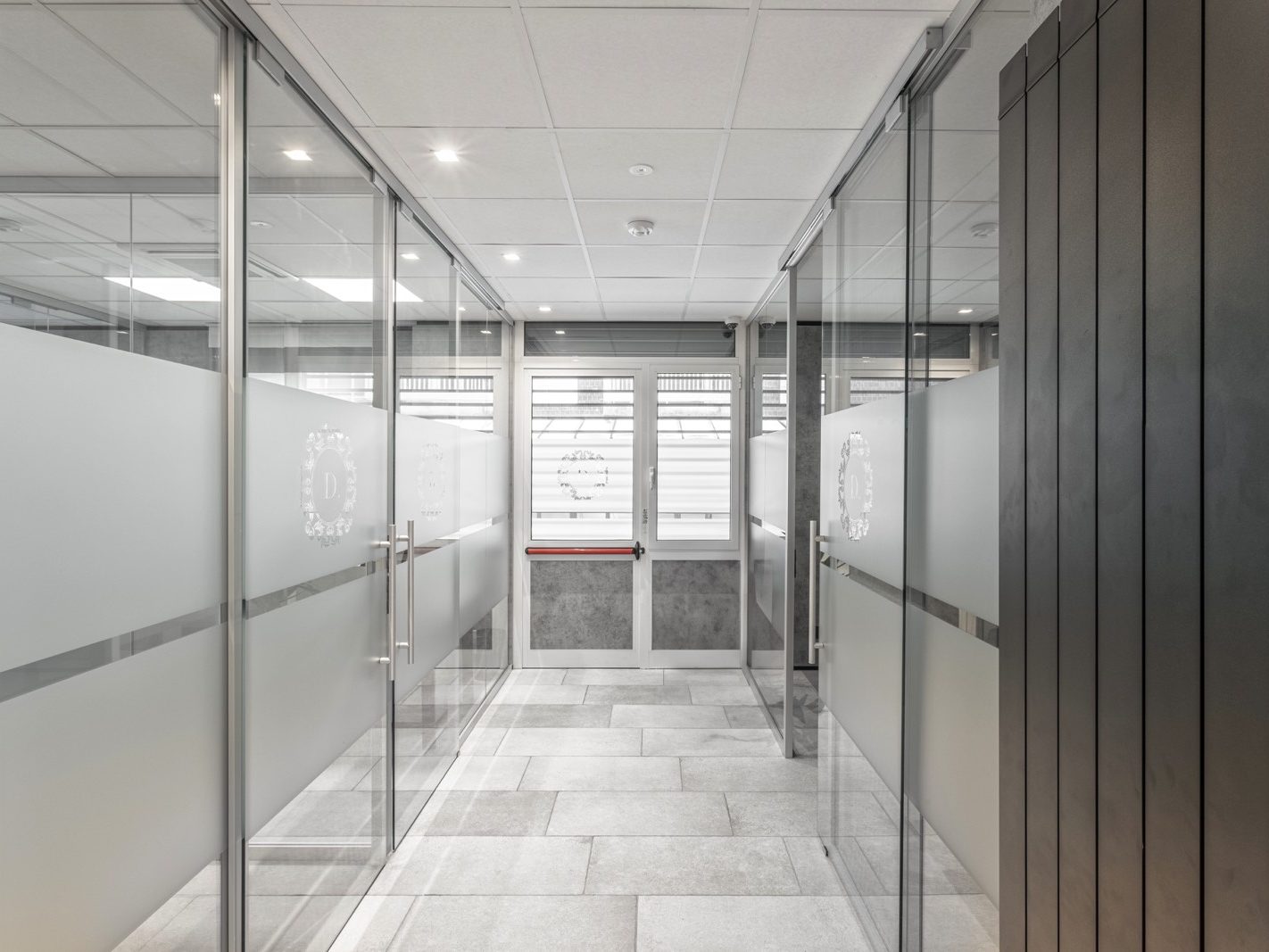 Corridoio tra gli Uffici. Una visuale del corridoio centrale tra gli uffici, dove le pareti Maisistem Glass creano una continuità visiva e spaziale. Il corridoio è illuminato da faretti incassati nel controsoffitto in fibra, che contribuiscono a un'illuminazione uniforme e piacevole.