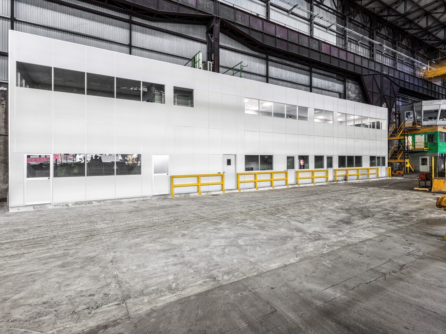 L'uso di pannelli modulari conferisce all'intera struttura un aspetto uniforme e pulito. Si nota anche una passerella gialla che aggiunge un tocco di colore e serve come percorso sicuro per i dipendenti. Il contesto industriale circostante è ben visibile, sottolineando la posizione operativa dell'azienda.