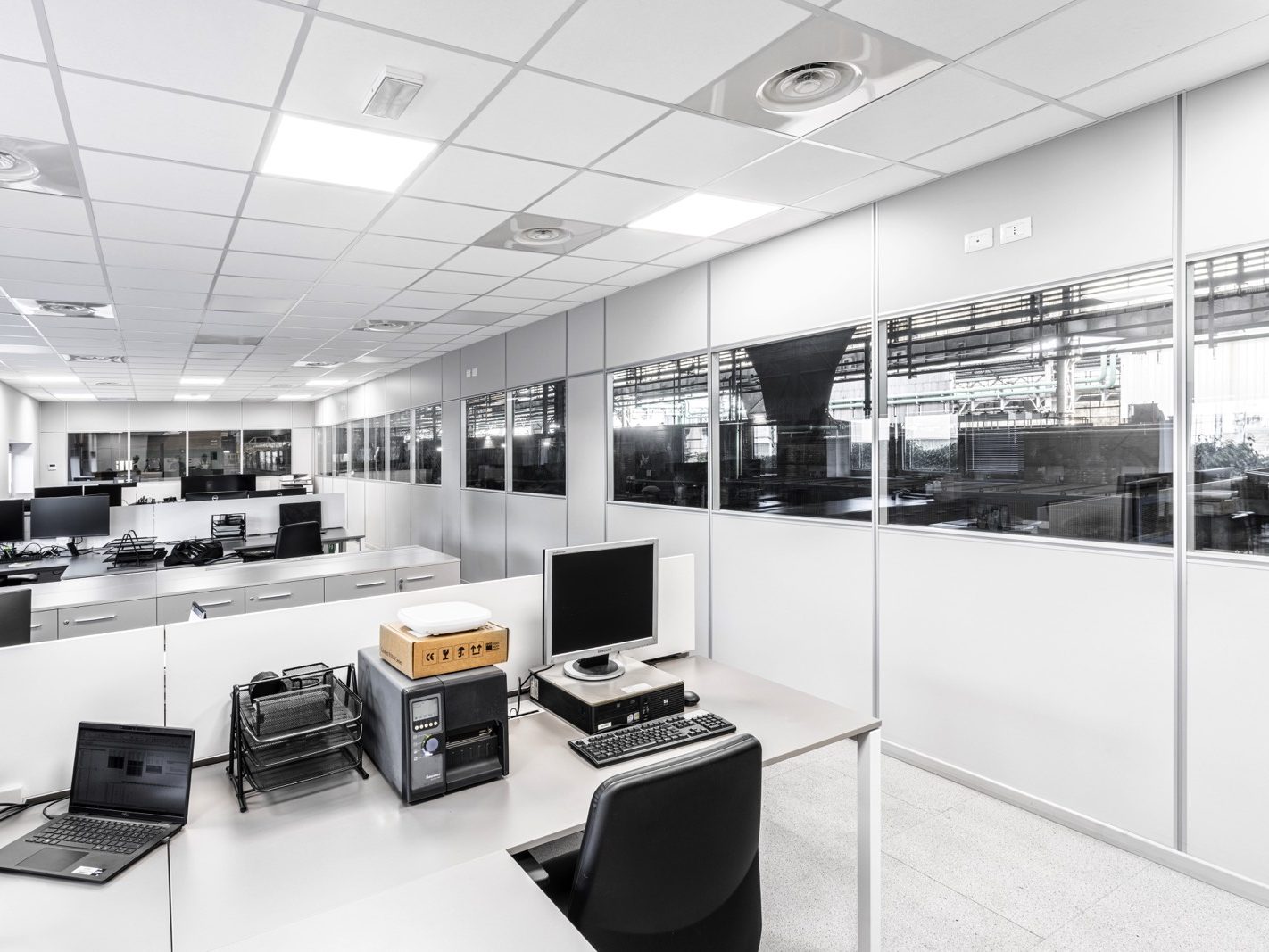 All'interno, gli uffici sono progettati per massimizzare l'efficienza e il comfort. Le pareti divisorie con ampie vetrate permettono di mantenere un ambiente luminoso e aperto, mentre separano gli spazi di lavoro individuali. Le postazioni sono moderne e ben attrezzate, garantendo un ambiente di lavoro produttivo.