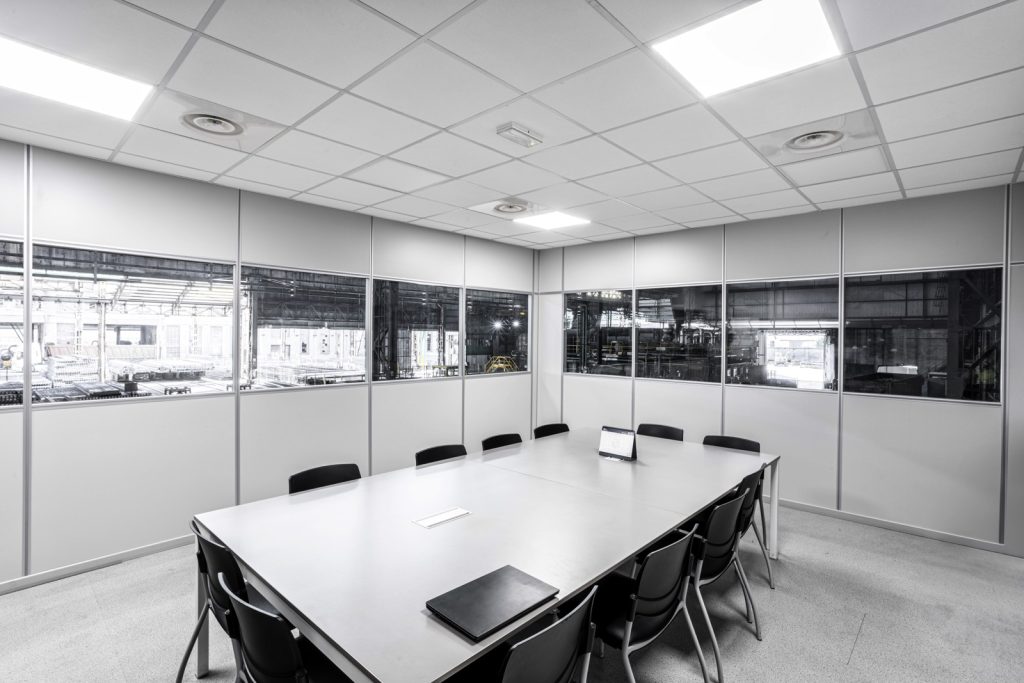 La sala riunioni è spaziosa e ben illuminata, con grandi finestre che offrono una vista sull'area di produzione. L'arredamento è minimalista, con un grande tavolo centrale e sedie confortevoli, ideali per riunioni di gruppo e sessioni di brainstorming. Le pareti divisorie con finestre permettono di mantenere un collegamento visivo con l'esterno, promuovendo un senso di trasparenza e collaborazione.
