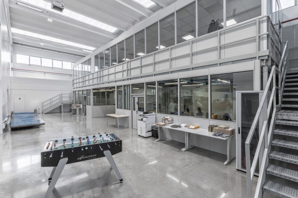 Le pareti divisorie modulari in vetro creano un ambiente aperto e luminoso. Una scala in metallo che conduce al piano superiore.