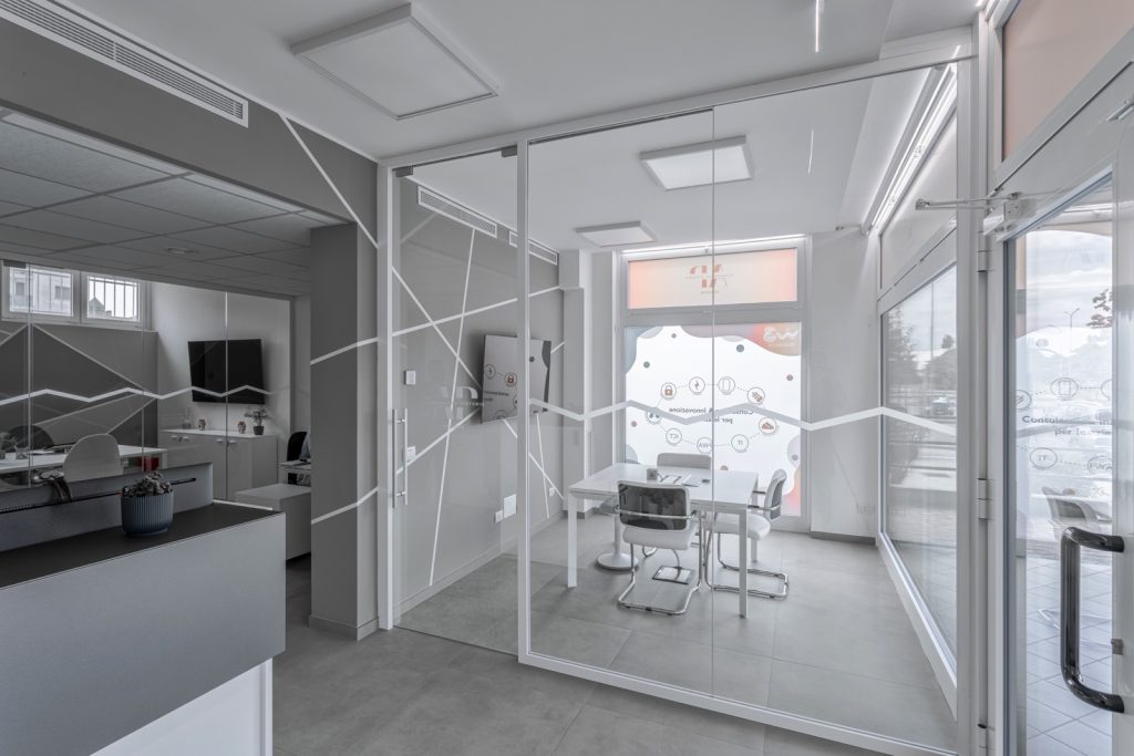 Le pareti in vetro con decorazioni geometriche forniscono un tocco di modernità e stile, mentre l'arredamento bianco dona un senso di ordine e pulizia. La luce naturale entra attraverso le ampie finestre, creando un ambiente luminoso e accogliente.