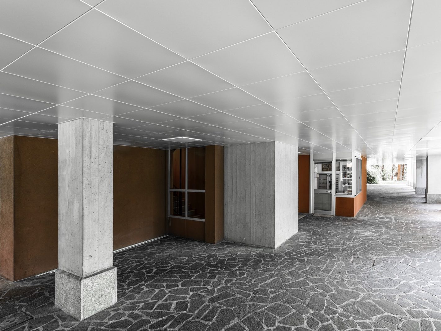 Un dettaglio del soffitto metallico che evidenzia la qualità della verniciatura e la precisione nell'installazione dei pannelli. La pavimentazione in pietra naturale sottolinea l'estetica elegante e funzionale dell'area.