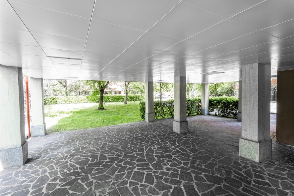 Un'altra vista dell'area di passaggio coperta che mette in evidenza la continuità del design e l'armonia tra soffitti e pavimenti. Si nota anche la vegetazione circostante, che contribuisce a creare un ambiente accogliente e rilassante.